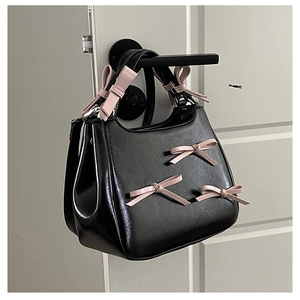 Detail of black glossy handbag featuring five soft pink 3D ribbon bows on the handle