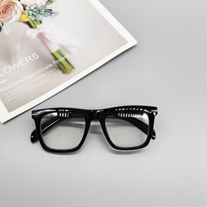 Close-up of black square frame glasses with metallic rivet detail on a stylish magazine
