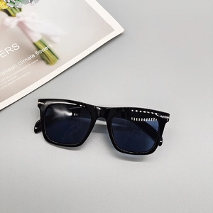 Flat lay of square black sunglasses with silver rivet accents on a grey surface
