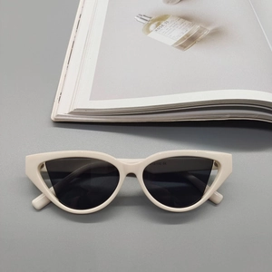 Detail view of cream cat-eye sunglasses with dark lenses on a minimalist magazine background