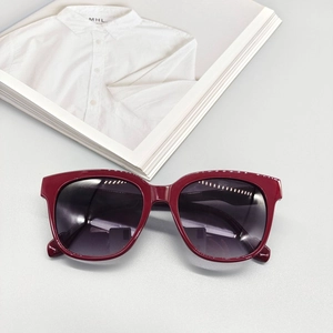 Detail of burgundy thick frame oval sunglasses with dark gradient lenses on a fashion magazine