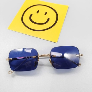 Vue à plat de lunettes de soleil carrées sans monture à verres bleus et pont en métal doré