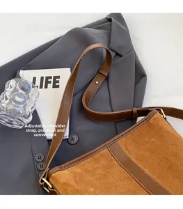 Detail of a brown suede bucket bag with adjustable strap on a grey blazer background