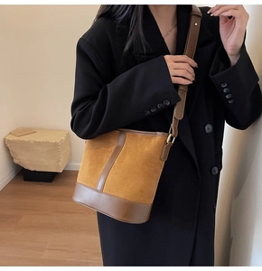 Close-up of brown suede bucket bag worn by model over a black blazer for a retro look