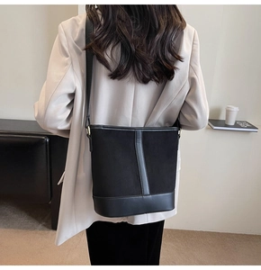 Detail of minimalist black bucket bag with mixed textures worn by a model in a modern room