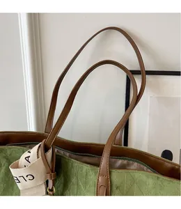 Close-up of green suede tote bag showing brown leather strap and metal zipper detail