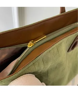 Detail of green suede tote bag with brown leather trim and golden metal zipper hardware