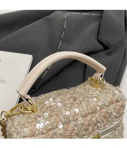 Close-up of tweed lipstick bag with white sequins and leather handle on a grey blazer