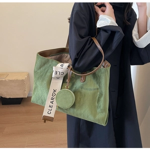 Detail of green oversized quilted tote bag with brown straps and white logo ribbon