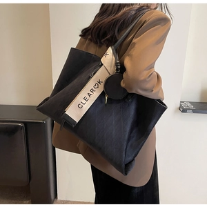 Detail of black quilted tote bag with wide canvas strap and round coin purse attachment