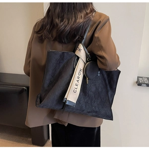 Detail of black quilted tote bag with velvet texture and decorative silk scarf strap accessory