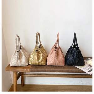 Detail of four woven tote bags in beige, gold, pink and black on a wooden bench
