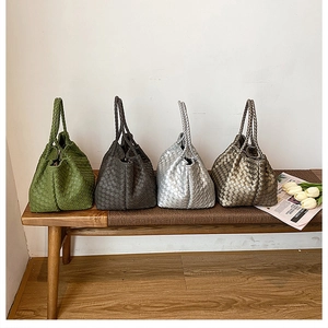 Detailed view of woven leather handbags in green, grey, silver and bronze on a bench