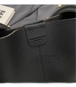 Détail du cuir grainé noir avec rivets dorés et logo gaufré sur le sac