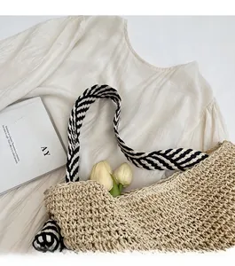 Detail of hand-woven straw tote bag with black and white striped rope strap on white cloth