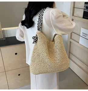 Détail d'un sac cabas en paille avec bandoulière rayée et décoration de nœud en ruban