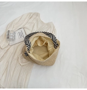 Detail of handwoven straw beach bag with striped trim and interior lining on white shirt