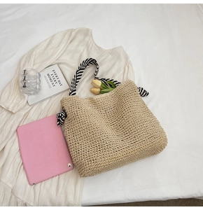 Detail of hand-woven straw tote bag featuring black and white striped knotted handles