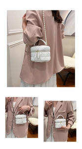 Detail view of a white heart-quilted mini box bag with gold chain strap and top handle