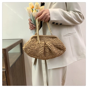 Detail of a beige woven cloud bag with gold chain strap held by a model in a minimal suit