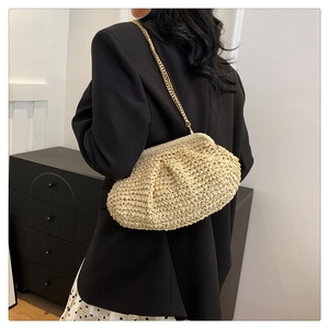 Detail of hand-woven straw cloud bag with elegant gold metal chain strap on model