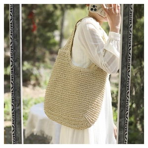Détail de la texture tressée d'un grand sac à bandoulière en paille beige en selfie