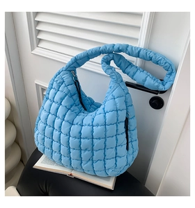 Detail of light blue quilted puff bag showing soft puffy texture and wide shoulder strap