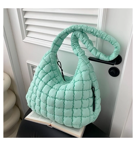 Detail of mint green quilted cloud bag with padded shoulder strap on a black chair