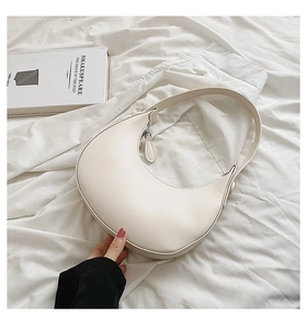 Minimalist creamy white PU leather hobo bag on soft white fabric with a vintage book