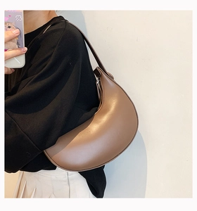 Close-up of a caramel half-moon faux leather shoulder bag worn under the arm style