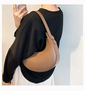 Close-up of brown semi-circle underarm bag with smooth faux leather and round metal buckle