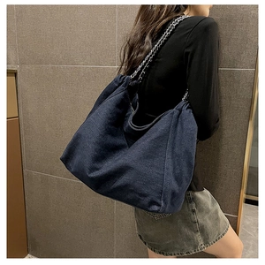 Detailed view of large dark blue denim tote bag with silver chain strap on model