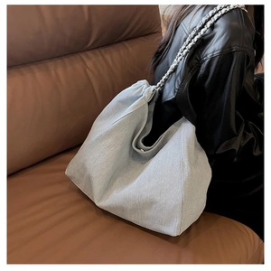 Light blue denim hobo bag with silver chain strap shown worn on person over leather jacket