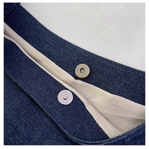 Detail of blue denim tote bag featuring magnetic closure and beige herringbone lining
