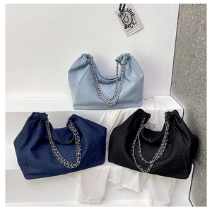 Three denim tote bags in blue and black with metallic chain straps on minimalist podium