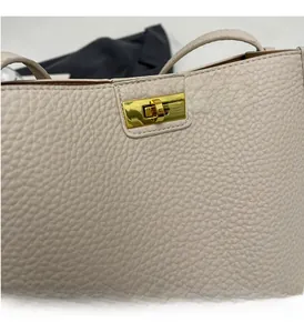 Dettaglio della serratura in metallo dorato e pelle con trama a litchi su borsa beige