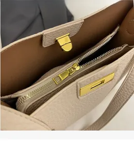 Detalle de la cremallera dorada y textura de cuero granulado en el bolso crema