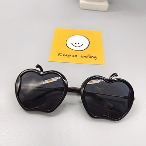 Detail of apple-shaped kids sunglasses with black frames and metal bridge on a card