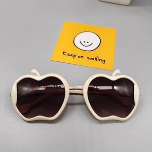 Detail of apple-shaped cream white frames and dark tinted lenses on kids' sunglasses