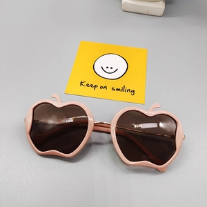 Detail of pink apple-shaped children's sunglasses with dark lenses and golden metal hinges