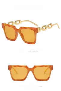 Detail of square amber sunglasses featuring yellow lenses and golden metal chain temples