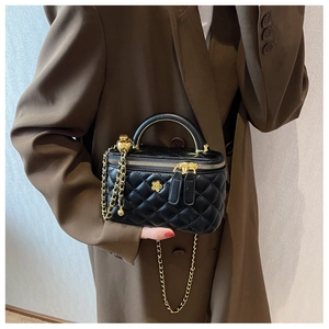 Detail of black quilted box bag with gold camellia charm and chain strap on a model