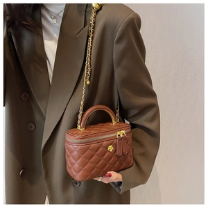 Detail of a brown quilted vanity box bag with gold chain strap and floral accent