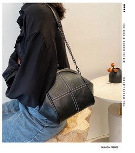 Detail of black pebbled leather shell bag with white contrast stitching and chain strap
