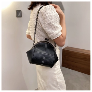 Close-up of black shell bag featuring white contrast stitching and vintage kiss-lock closure