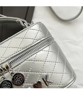 Détail du sac bandoulière argenté matelassé avec pendentif cœur et breloque fleur