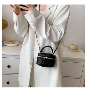 Close-up of black quilted PU leather mini handbag with gold chain strap on white blazer