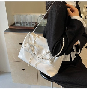 Détail d'un sac cabas en cuir verni blanc avec nœuds et bandoulière chaîne argent