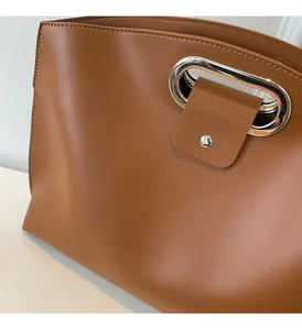 Detail of brown leather handbag featuring sleek silver oval metal handle and magnetic closure