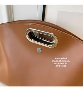 Detail of minimalist leather tote showing oval metal handle and magnetic snap closure
